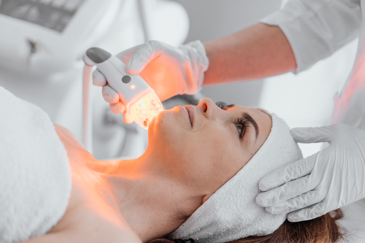 The beautician applies light led therapy to rejuvenate and regenerate the patient's facial cells. A young woman is relaxed at a reception at a cosmetologist at a beauty clinic.