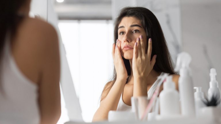 Woman Touching Face Looking At Skin In Mirror