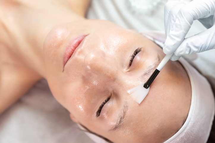 Close-up beautician doctor hand making anti-age procedure apply peeling acid young attractive female client at beauty clinic. Cosmetologist specialist doing skincare treatment. Health care therapy.