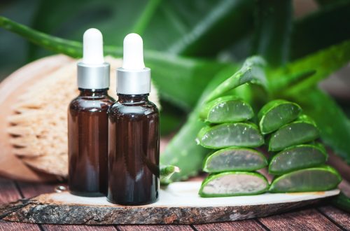 Aloe oil ,  massage brush juicy scarlet cut into pieces on a natural wooden background . Organic bio anticellulite cosmetics