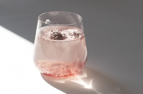 Glass of natural strawberry collagen protein powder in glass of water for skin regeneration. Trendy food additives. White background with sunlight and deep shadow of glass. Hard sunlight.