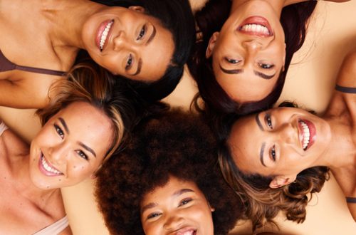 Beauty, above and portrait of a diversity of women with smile for skincare isolated in a studio brown background together. Support, happy and group of friends with care laying on floor for skin